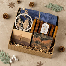 Load image into Gallery viewer, Menβs holiday gift box featuring two artisan soap bars, one marbled, one layered. A wooden soap tray, navy cotton towel, laser-cut Santa ornament, and a Merry Christmas tag, all nestled in eco-friendly kraft packaging.