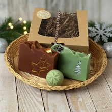 Load image into Gallery viewer, A kraft box with a transparent lid filled with brownish soap, tied with a festive white, red, and green rope and adorned with a 'Merry Christmas' sticker. Beside the box are brownish square soap, green square soap, and a round pale green mini soap.