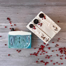Load image into Gallery viewer, Four artisan Christmas soaps displayed on wood with red berries. Emerald green swirls with snowy white tops decorated with pinecones and botanicals, festive handmade holiday gift bar.