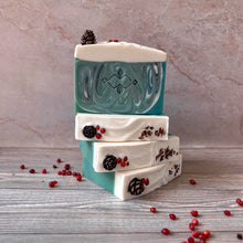 Load image into Gallery viewer, Stack of vegan Christmas tree soap bars with green swirled fronts and snowy white tops. Each bar decorated with pinecones and red berries, festive handmade winter gift soap