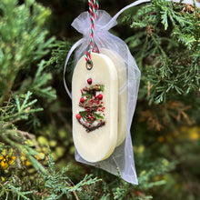 Load image into Gallery viewer, An elongated oval white wax tablet embellished with tiny dried branches, cranberry seeds, and red peppercorns resembles a Christmas tree. It features a red and green decorative rope threaded through a metal eyelet. Packaging: white organza bag.