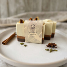 Load image into Gallery viewer, Front-facing artisan spiced orange soap bar with label reading "Savon Artisanal – Artisan Soap," featuring warm holiday colors and natural decor like cinnamon and orange, ideal for festive gifting and winter body care.