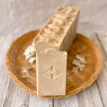 Load image into Gallery viewer, Off-white, tall soap bar with white swirls, a textured top, and a company stamp on the surface.