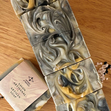 Load image into Gallery viewer, A soap with distinct white, black, and yellow layers, featuring a textured top. The soap bar is labeled and wrapped with recyclable paper for an eco-friendly touch.