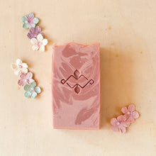 Load image into Gallery viewer, Powdery rose-colored tall soap bar with pale-rose swirls and a wavy textured top. It features a Woods and Mosses company stamp on its surface.