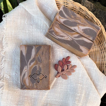 Load image into Gallery viewer, Two handcrafted soap bars with a marbled caramel and chocolate design are placed on a beige cloth. One bar features a stamped Woods and Mosses logo while the other showcases smooth swirls.