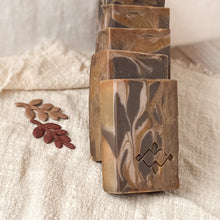 Load image into Gallery viewer, 4 handcrafted, rectangular soap bars with a marbled caramel and chocolate design, sitting on a textured beige fabric. The soap bars have a smooth, swirled pattern with a Woods and Mosses stamped logo on the surface, giving them an artisanal look.