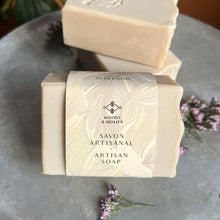 Charger l'image dans la galerie, A creamy off-white artisan soap bar with a slightly textured top edge. One bar is wrapped in elegant packaging with a soft botanical design, featuring the brand name Woods and Mosses and the words Savon Artisanal – Artisan Soap. Another unwrapped bar is embossed with a lamb logo.