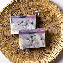 Load image into Gallery viewer, Handcrafted natural soap bar with a marbled swirl of white, lilac, and deep purple, accented with a Woods and Mosses Logo. The top features a smooth purple layer with a hint of shimmer. Elegant and artistic, designed for floral scent lovers and gentle skincare.