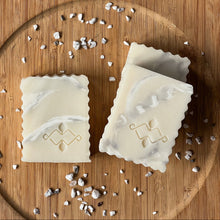 Load image into Gallery viewer, A close-up of two natural soap bars with a soft marble swirl pattern, scalloped edges, and a central stamped Woods and Mosses logo.