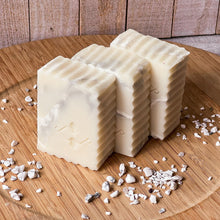 Load image into Gallery viewer, A handcrafted rectangular soap bar with a white and light gray marble swirl pattern, scalloped edges, and an embossed geometric Woods and Mosses logo on the front.