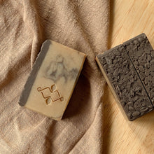 Load image into Gallery viewer, Natural handmade coffee soap bars with dark textured tops and marbled tan bases, featuring an embossed Woods and Mosses logo on the side.