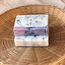Load image into Gallery viewer, Handcrafted natural soap bar with a marbled swirl of white, lilac, and deep purple, accented with a Woods and Mosses Logo. The top features a smooth purple layer with a hint of shimmer.