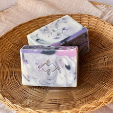 Load image into Gallery viewer, Handcrafted natural soap bar with a marbled swirl of white, lilac, and deep purple, accented with a Woods and Mosses Logo. The top features a smooth purple layer with a hint of shimmer. Elegant and artistic, designed for floral scent lovers and gentle skincare.