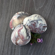 Load image into Gallery viewer, A soap bar shaped like a rock with white, brown, and dark violet swirls.