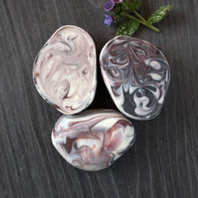 Load image into Gallery viewer, A soap bar shaped like a rock with white, brown, and dark violet swirls.