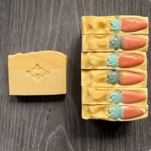 Load image into Gallery viewer, The square soap showcases a Woods and Mosses logo in the center. The soap body is yellow, while the top is a deeper shade of yellow, adorned with a small orange-green carrot decoration.