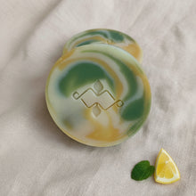 Load image into Gallery viewer, Round lemon and peppermint artisan soap bar with green and yellow swirls and embossed logo.