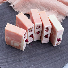 Load image into Gallery viewer, Lineup of five natural rose soap bars, each with soft marbled colors and dried rosebuds, showcasing the floral topping and minimalist cut edges.