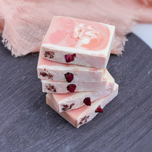Load image into Gallery viewer, Stack of artisan soap bars in a rose-pink swirl with embedded dried rosebuds and petal details, highlighting their handmade texture and shape.
