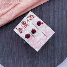 Load image into Gallery viewer, Top view of three floral soap bars with dried rosebuds and petals embedded on a creamy pink surface, featuring gentle marbled swirl and botanical decor.
