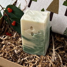 Load image into Gallery viewer, Cream and green Bay Leaf swirled artisan soap bar with botanical design, placed on kraft paper shred beside fabric pouch printed with green and brown trees.