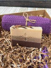 Load image into Gallery viewer, Front view of layered natural soap bar (beige and cocoa tones) standing in gift box with purple cloth backing.