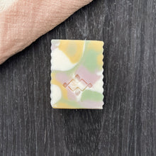 Load image into Gallery viewer, Single rectangular artisan soap bar with soft pastel swirls and textured edges, centered on a dark surface with a peach linen fabric in the corner.
