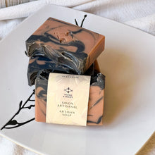 Load image into Gallery viewer, Handmade natural soap bar with peach and black swirl pattern, labeled as ‘Savon Artisanal Artisan Soap’ from Woods & Mosses, displayed on a white plate.