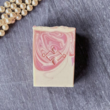 Load image into Gallery viewer, Top view of handmade pink soap bar with stamped design, styled with pearls on gray background.