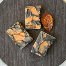 Load image into Gallery viewer, Handcrafted Autumn Ember Artisan Soap bar with a swirled black and orange autumn-inspired design, presented on a round dark wood tray. - vegan, handmade, moisturizing cleanser, eco-friendly gift idea from Woods and Mosses.