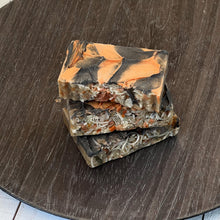 Load image into Gallery viewer, A stack of three natural handcrafted Autumn Ember Artisan Soap bars with orange and black swirled tops and visible botanical inclusions, displayed on a round dark wood tray. - vegan, handmade, moisturizing cleanser, eco-friendly gift idea