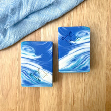 Load image into Gallery viewer, Ocean Wave handmade by Woods and Mosses soap bar with blue and white swirl pattern, placed on a light wooden surface.