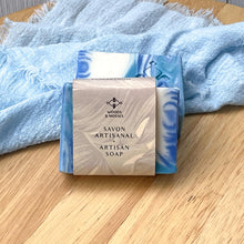 Load image into Gallery viewer, A blue and white swirl handcrafted soap bar with a 'Savon Artisanal Artisan Soap' label, displayed on a light wood tray.