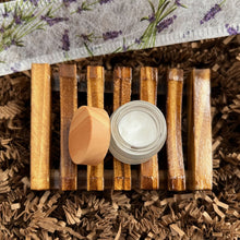 Load image into Gallery viewer, Luxury Lavender Spa Gift Basket, Christmas Edition by Woods and Mosses: Opened glass jar on a wooden soap dish containing white eye cream.