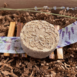 Luxury Lavender Spa Gift Basket, Christmas Edition by Woods and Mosses: Dark beige, round shampoo bar featuring a textured surface and a delicate flower design.