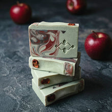 Load image into Gallery viewer, Stack of marbled soap bars with red swirls on a dark surface with apples in the background