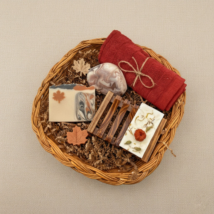 Canadian self care gift box with handmade natural soaps, wooden soap dish, red towel, and maple leaf decorations arranged in a wicker basket.