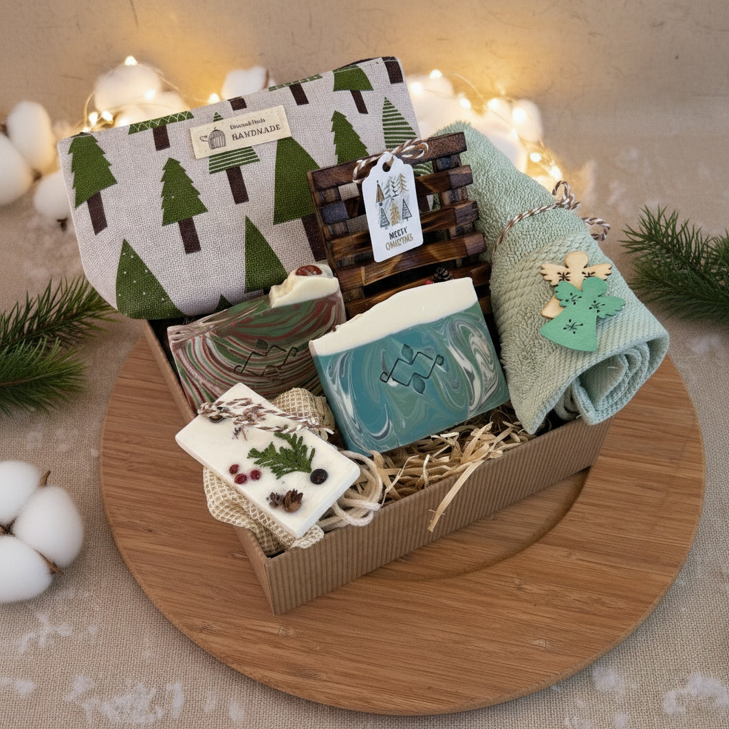 Vegan Christmas gift box with handmade natural soaps, wooden soap dish, green towel, and holiday pouch in eco-friendly packaging, displayed with pine branches and festive lights on a wooden tray.