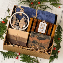 Load image into Gallery viewer, Men’s holiday gift box featuring two artisan soap bars, one marbled, one layered. A wooden soap tray, navy cotton towel, laser-cut Santa ornament, and a Merry Christmas tag, all nestled in eco-friendly kraft packaging.