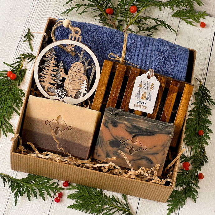 Men’s holiday gift box featuring two artisan soap bars, one marbled, one layered. A wooden soap tray, navy cotton towel, laser-cut Santa ornament, and a Merry Christmas tag, all nestled in eco-friendly kraft packaging.