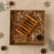 Load image into Gallery viewer, Brown slatted wooden soap dish inside a kraft gift box with paper filler and pinecones.