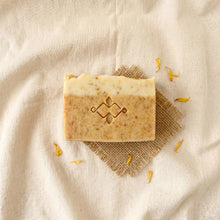 Load image into Gallery viewer, Single calendula turmeric soap bar with two-tone layers, botanical speckles, and carved front logo