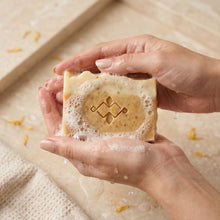 Load image into Gallery viewer, Calendula turmeric soap bar with creamy lather over a stamped Woods and Mosses brand logo
