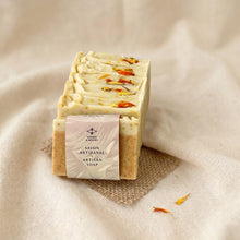 Load image into Gallery viewer, Wrapped calendula turmeric soap bar with matching unwrapped bars showing flower-topped cream layers