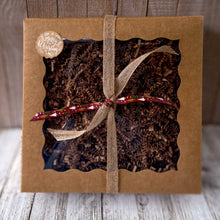 Load image into Gallery viewer, Brown kraft gift box with a clear window, filled with raffia paper and tied with brown and red ribbon. Features a Merry Christmas decorative sticker.
