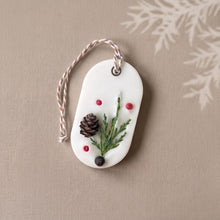 Charger l'image dans la galerie, White oval soy wax sachet with hanging cord, evergreen sprig, mini pinecone, and red botanical accents