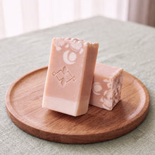 Load image into Gallery viewer, Two blush-peach collagen soap bars with cream base, white floral pattern, stamped logo, and handmade speckled finish