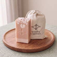 Load image into Gallery viewer, Blush peach collagen soap bar with cream base, white floral pattern, stamped logo, and Woods &amp; Mosses muslin gift bag.