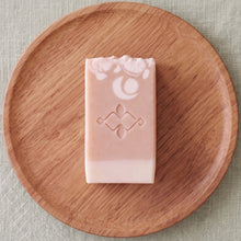 Load image into Gallery viewer, Flat lay of one collagen soap bar with blush-peach body, cream base, white floral detail, and stamped center Woods and Mosses logo